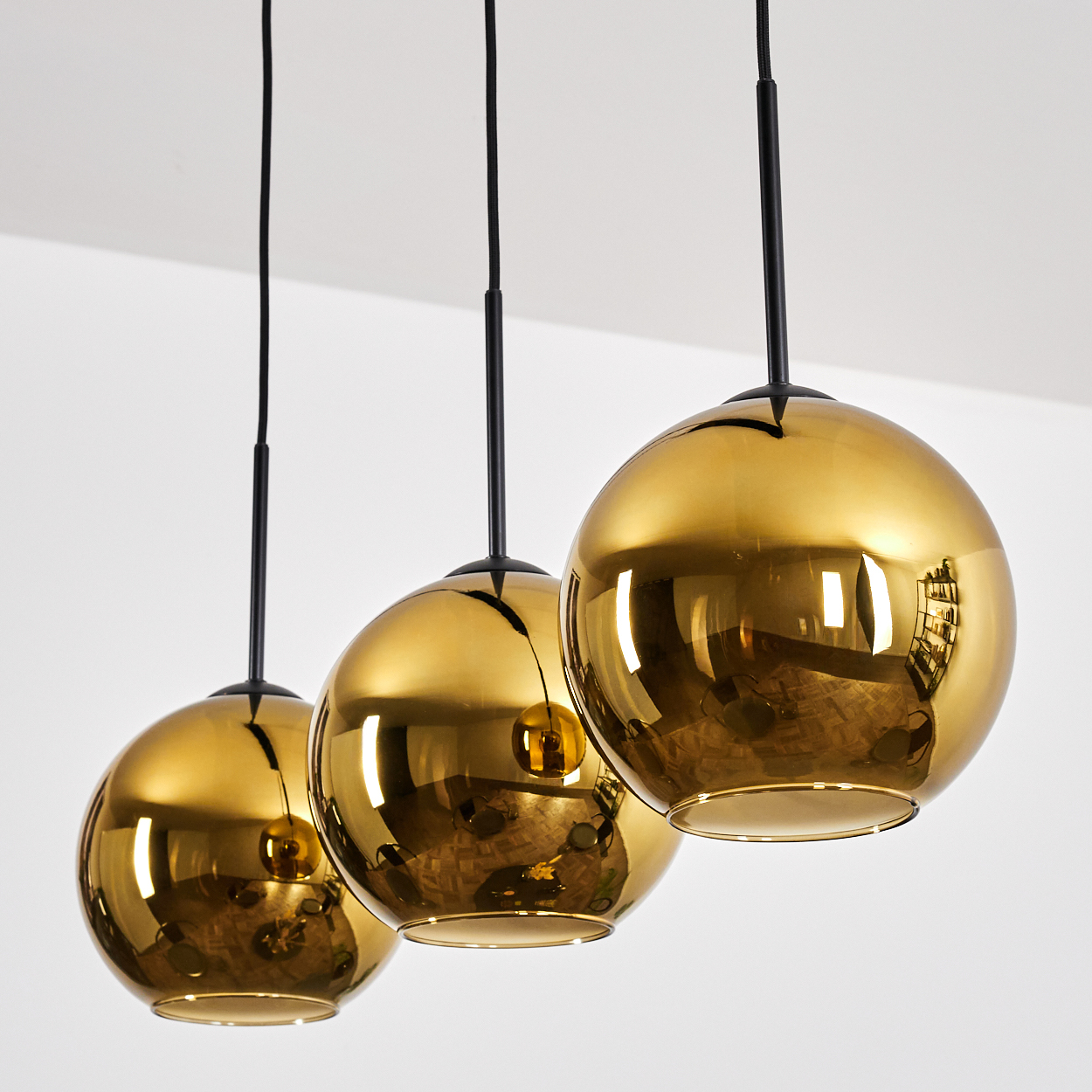 Drei goldene Pendelleuchten hängen von der Decke. Jede hat einen kugelförmigen Schirm, der den Raum reflektiert. Schwarze Kabel und Armaturen.