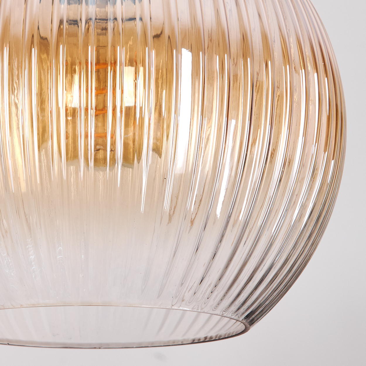 Nahaufnahme einer Glasleuchte mit gerippter Textur. Das Glas ist bernsteinfarben, mit hellem Licht darin.