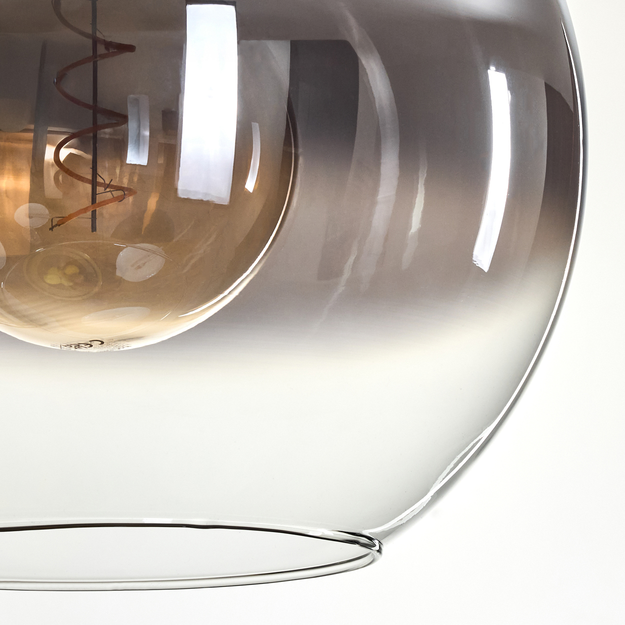 Nahaufnahme einer Glasleuchte. Sie zeigt eine Glühbirne mit Spiralfaden, die in einem getönten, mehrschichtigen Glasschirm eingeschlossen ist.