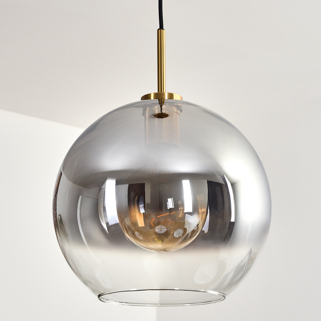 Eine moderne Pendelleuchte mit silber-grauem Glasschirm. Sie hat einen goldenen Stiel und eine sichtbare Glühbirne im Inneren.