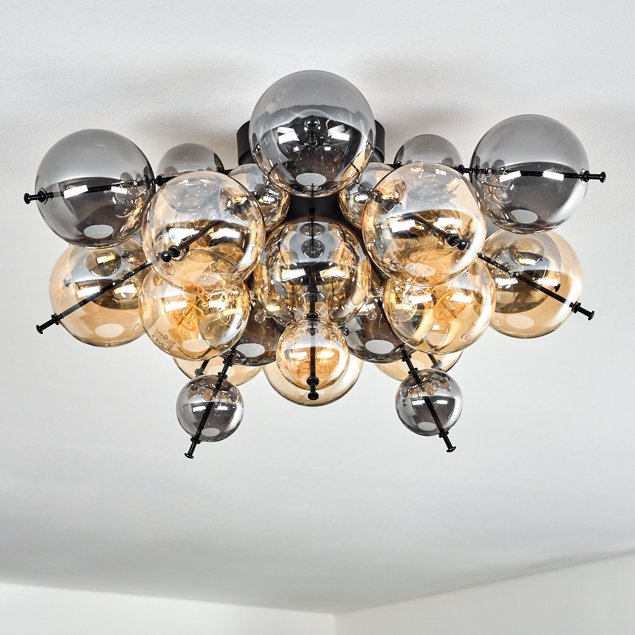 Eine moderne Deckenleuchte mit mehreren Glaskugeln in Gold und Grau, montiert auf einem schwarzen Rahmen. Weißer Hintergrund.