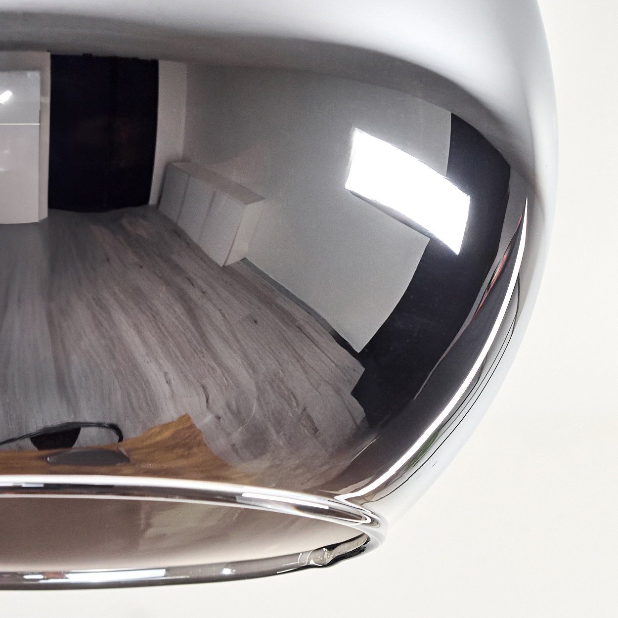 Ein reflektierendes Chromobjekt mit verzerrten Reflexionen eines Raumes. Der Raum hat helle Holzböden, weiße Wände und eine schwarze Tür.