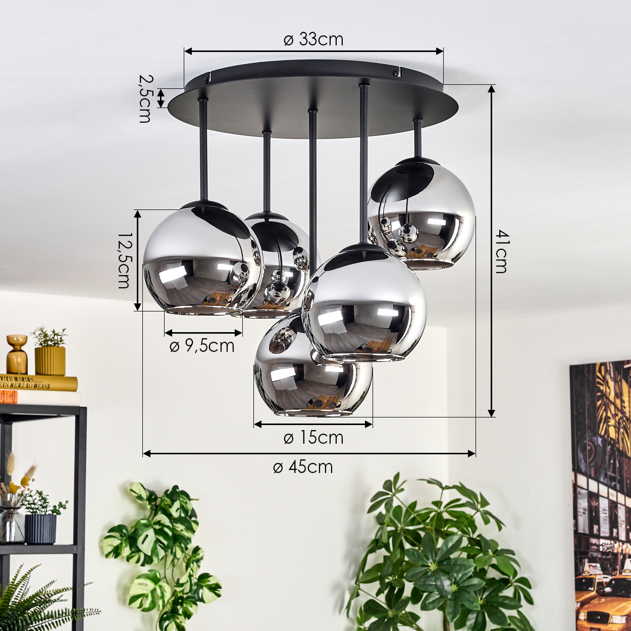 Eine moderne Deckenlampe mit fünf kugelförmigen Chromschirmen. Maße sind angegeben. Pflanzen und Regale sind im Hintergrund.