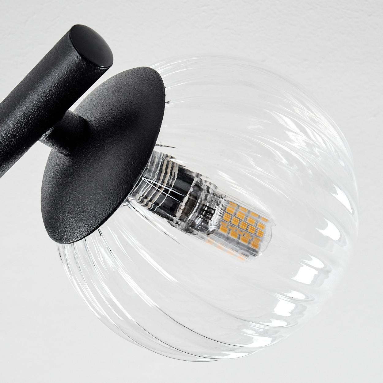 Nahaufnahme einer modernen Lampe. Sie hat einen klaren, gerippten Glaskolben mit einer Glühbirne und einem schwarzen Metallrahmen.
