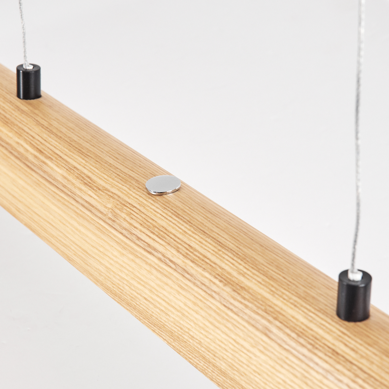 Nahaufnahme eines Holzbalkens mit Metallakzenten. Zwei schwarze Zylinder halten ihn. Eine kleine silberne Scheibe liegt auf dem Holz.