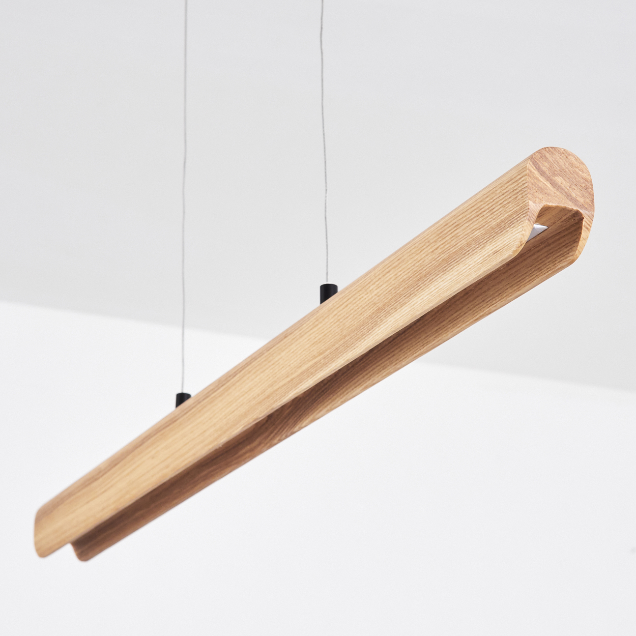 Eine moderne Holz-Pendelleuchte hängt von der Decke. Sie hat eine lange, hellbraune, gebogene rechteckige Form.