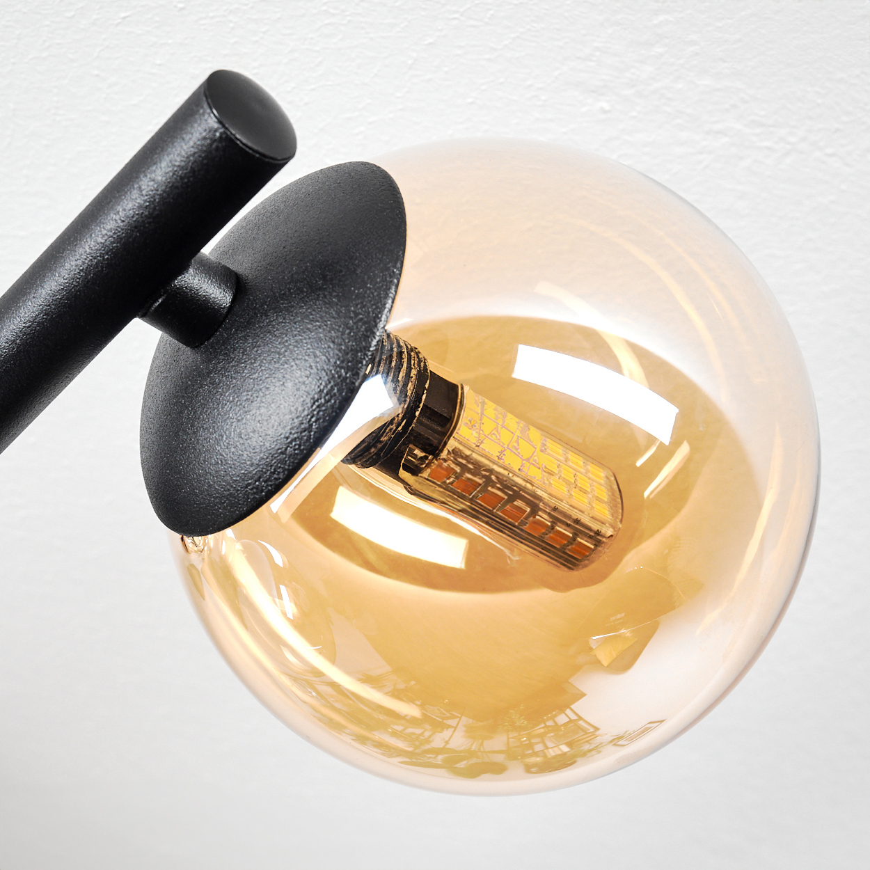 Nahaufnahme einer modernen Lampe mit schwarzem Arm und Glaskugel mit hellem LED-Licht. Weißer Hintergrund.