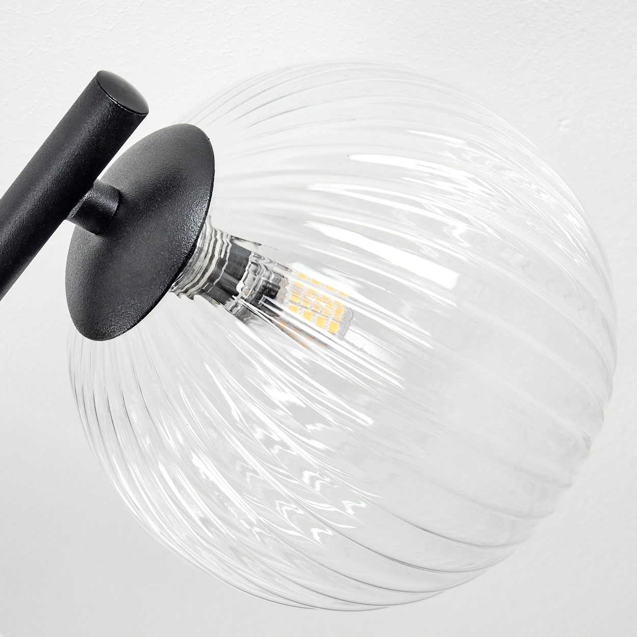 Nahaufnahme einer klaren Glaskugellampe mit schwarzem Metallarm. Die Lampe hat eine geriffelte Textur, mit einer warmen Glühbirne.