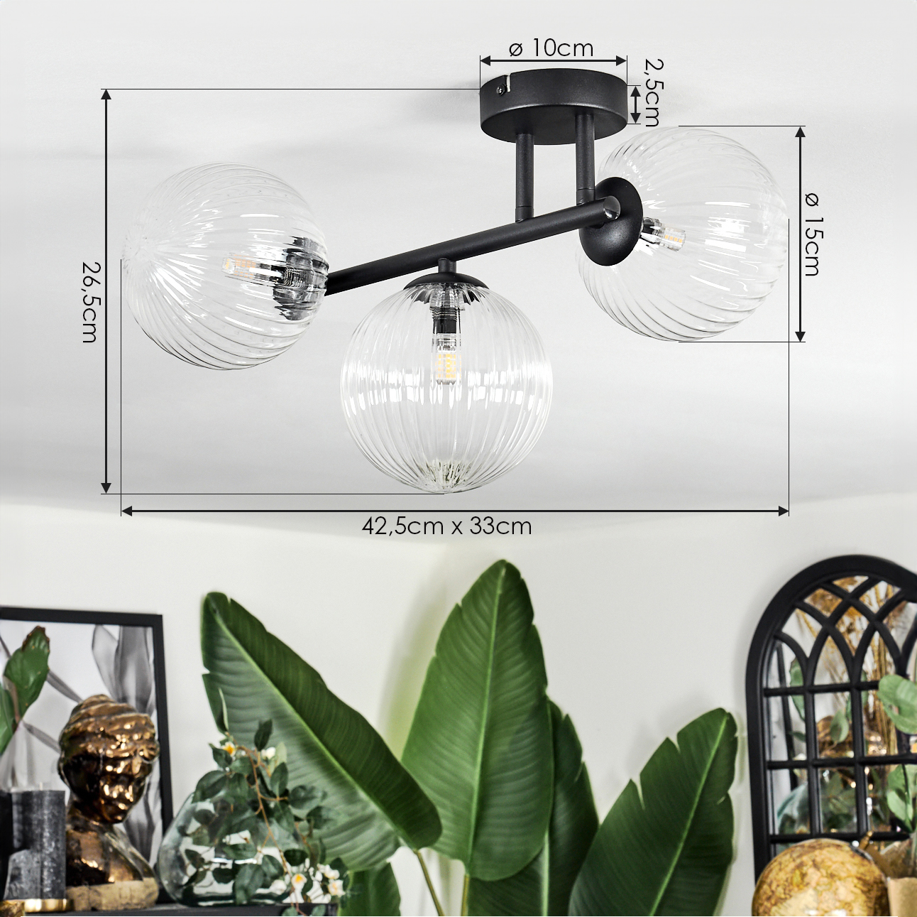 Eine moderne Deckenlampe mit drei Glaskugeln. Sie ist schwarz und hat Größenangaben. Pflanzen und Deko im Hintergrund.