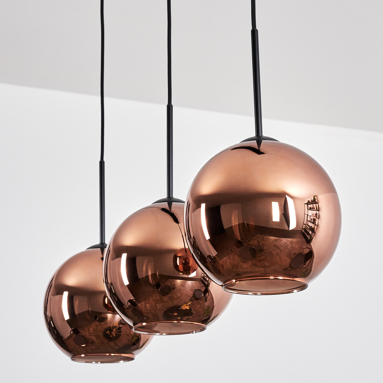 Drei kupferfarbene Pendelleuchten hängen an schwarzen Kabeln von einer weißen Decke. Die Leuchten sind kugelförmig und reflektierend.