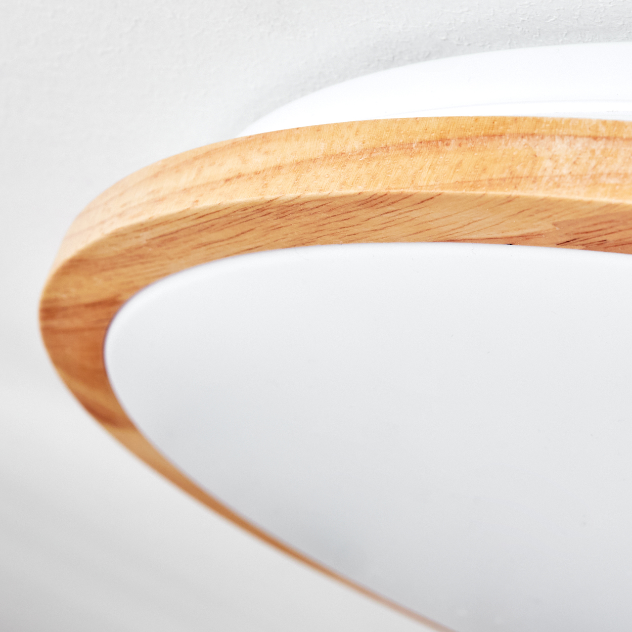 Nahaufnahme einer modernen Leuchte. Sie hat eine Holzverkleidung um einen weißen, abgerundeten Sockel auf weißem Hintergrund.