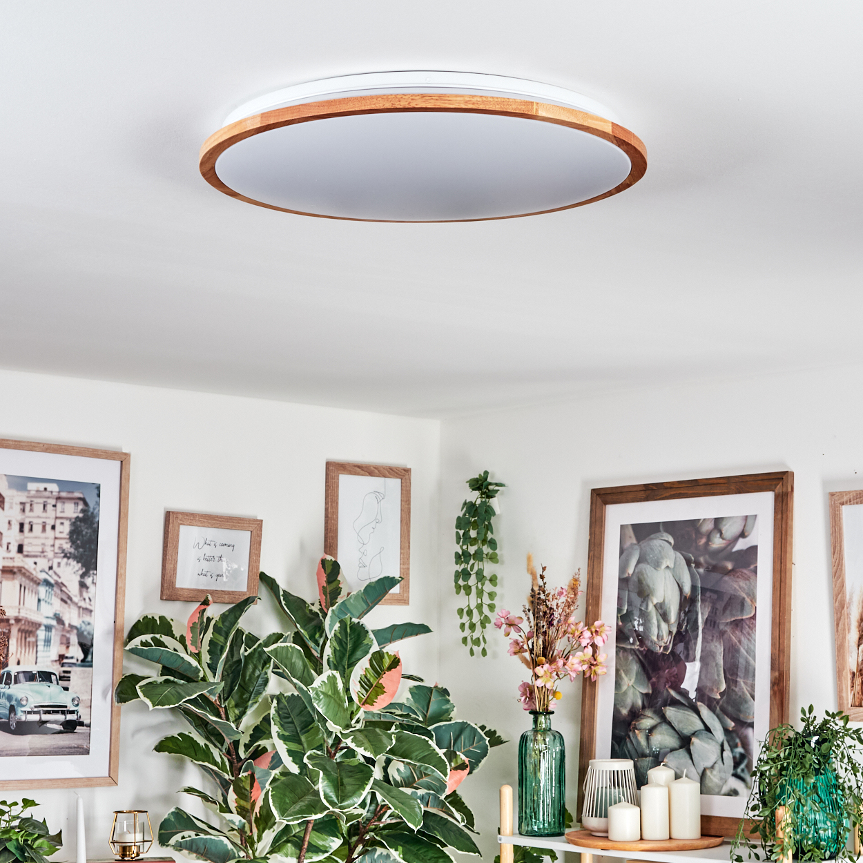 Ein modernes Wohnzimmer mit Deckenleuchte, Pflanzen, gerahmten Bildern und Kerzen auf einem Regal.