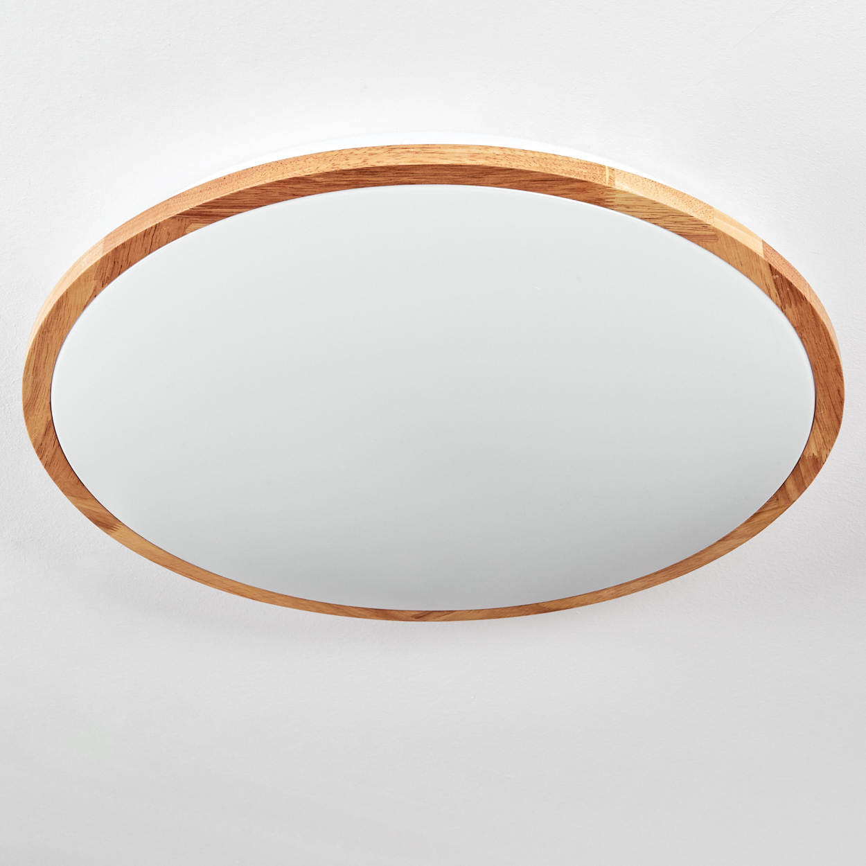 Ein ovaler Spiegel mit Holzrahmen an einer weißen Wand. Die Oberfläche des Spiegels ist klar und reflektiert den weißen Hintergrund.