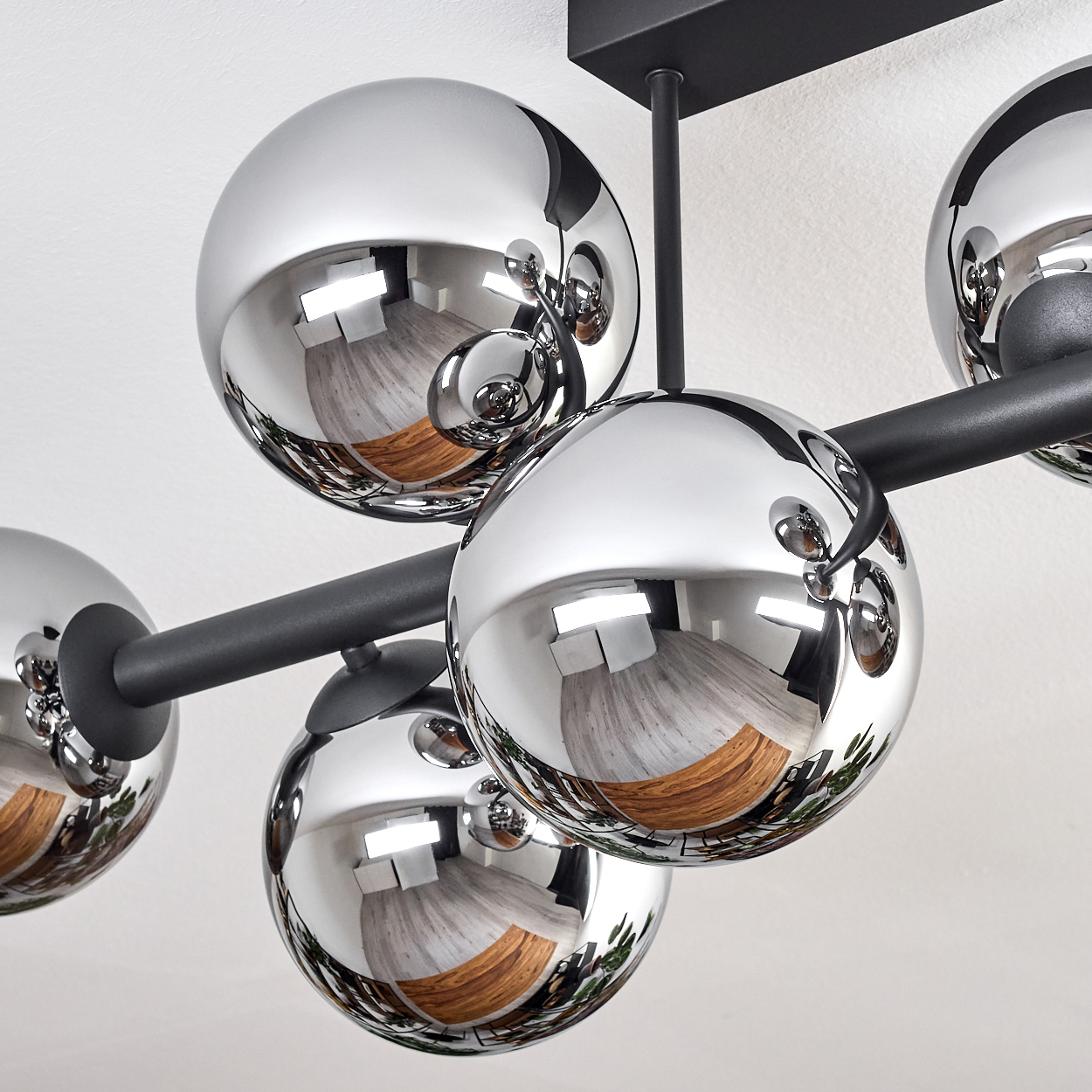 Nahaufnahme einer modernen Deckenleuchte mit verchromten Kugeln, die den Raum reflektieren. Schwarze Metallstruktur.