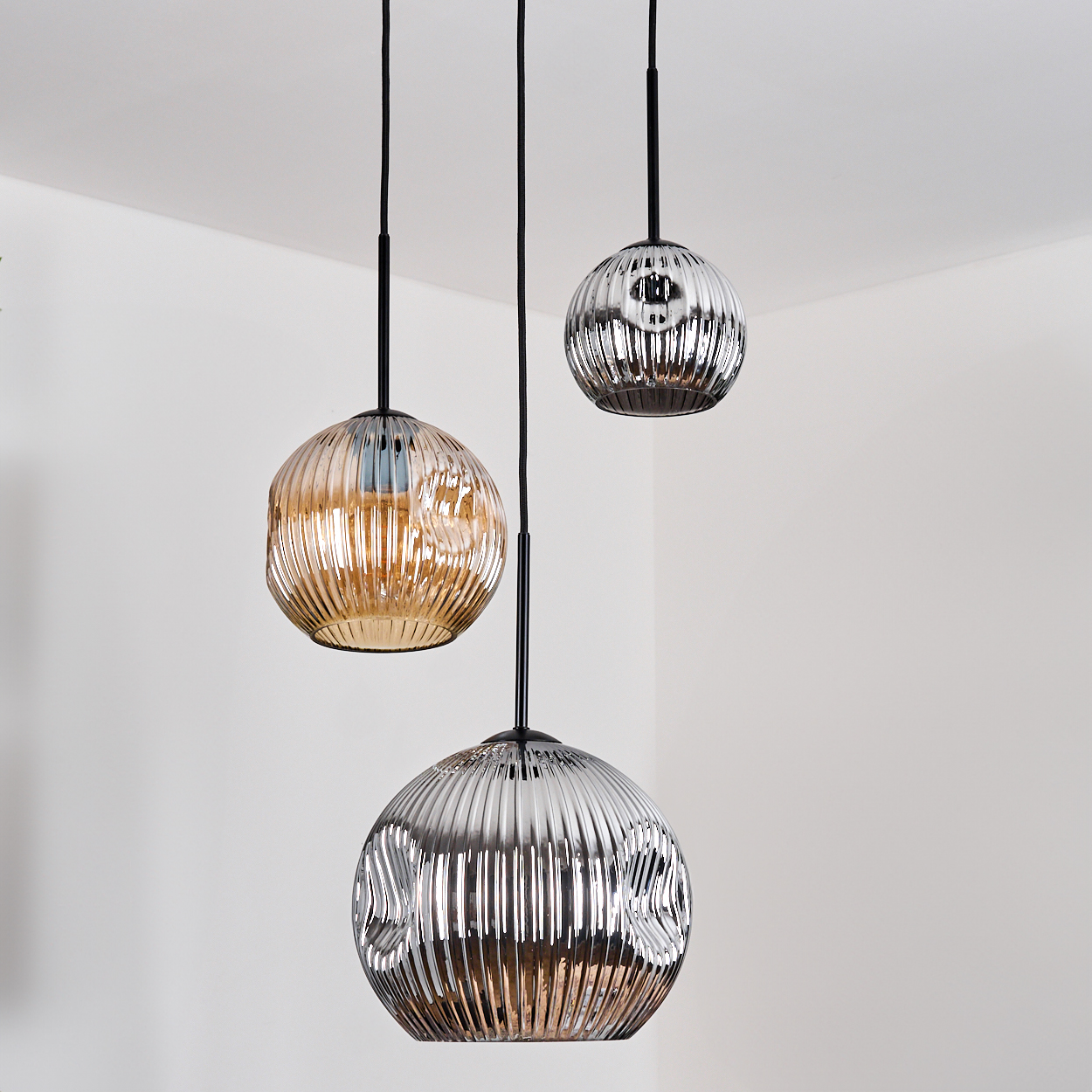 Drei kugelförmige Pendelleuchten mit geriffelten Glasschirmen hängen von der Decke. Die Schirme sind silber und gold.