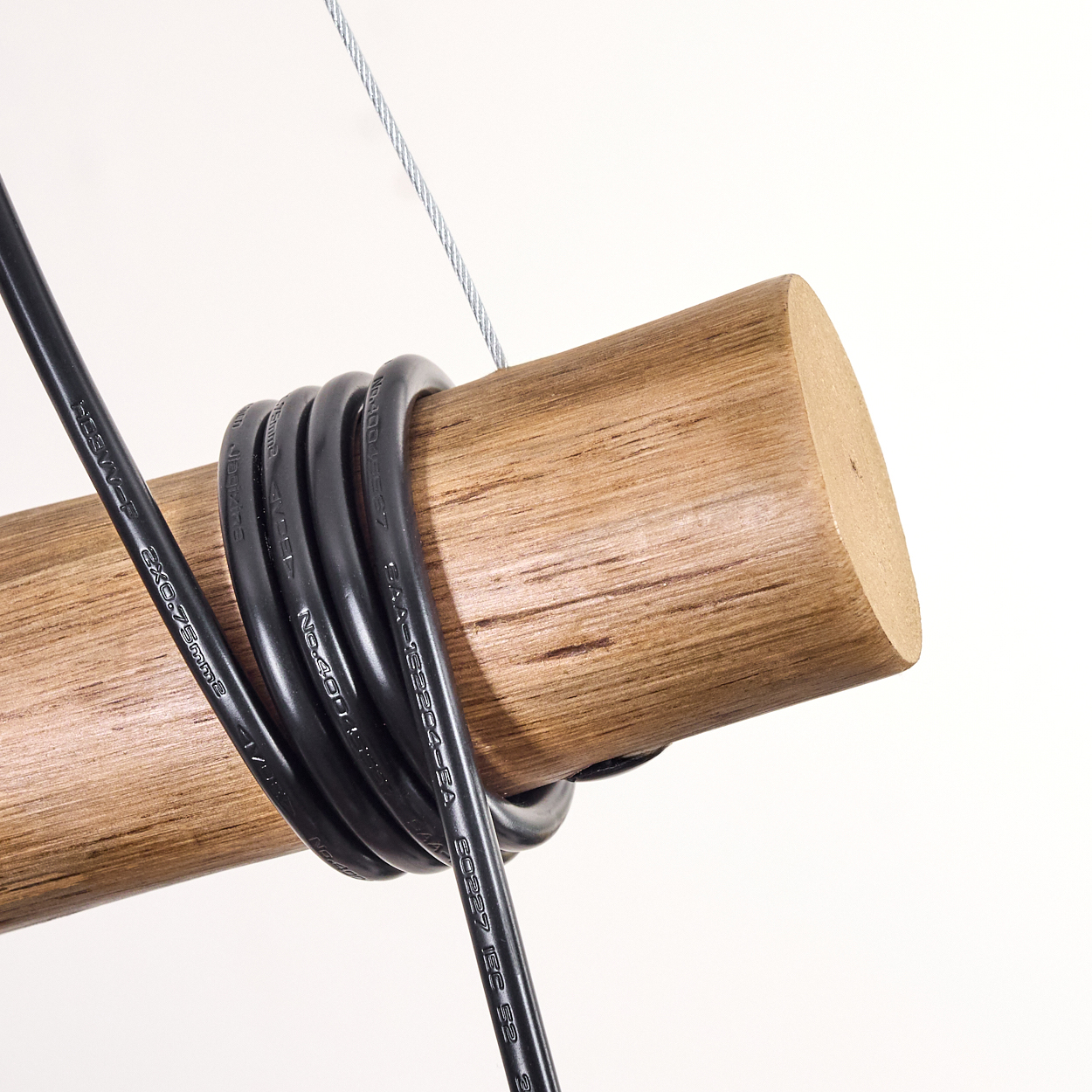 Ein Holzzylinder, um den schwarze Drähte gewickelt sind. Ein silbernes Kabel befindet sich darüber. Der Hintergrund ist weiß.