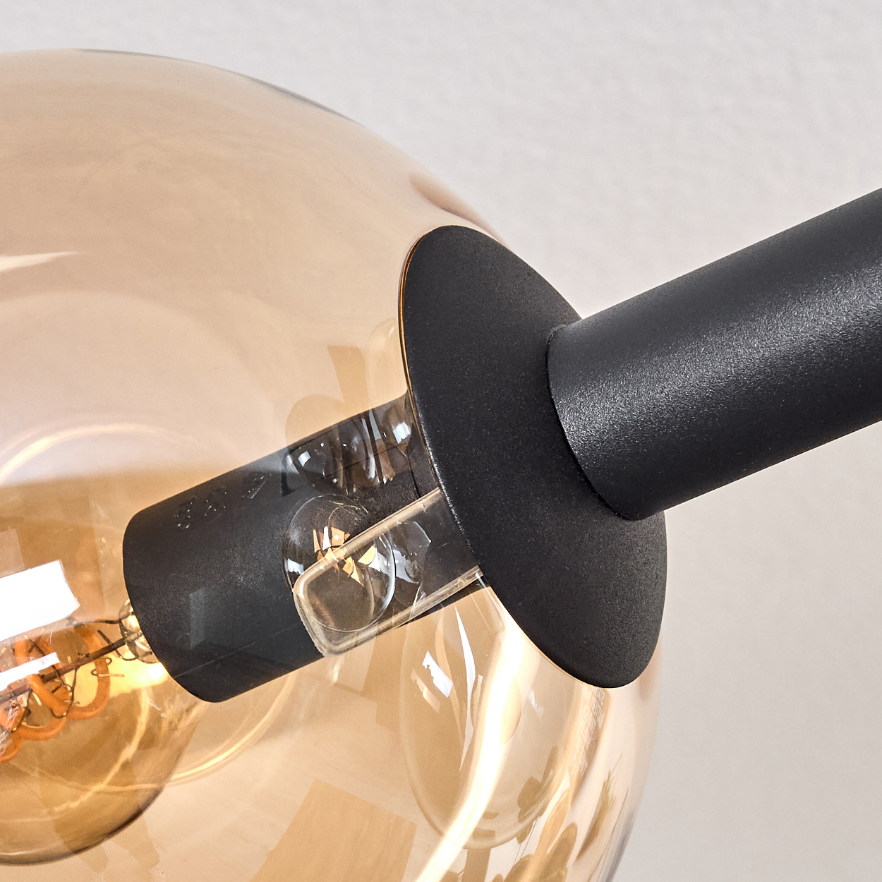Nahaufnahme einer modernen Lampe. Ein schwarzer Metallarm hält eine klare Glaskugel mit einer leuchtenden, orangefarbenen Glühbirne.