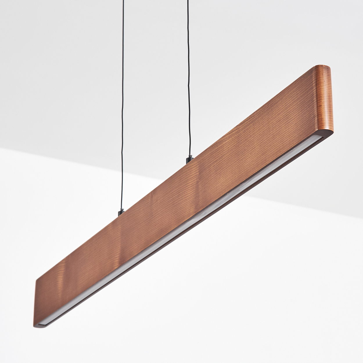 Eine rechteckige Holzlampe wird von der Decke mit zwei schwarzen Drähten abgehängt. Sie hat einen Lichtstreifen auf der Unterseite.