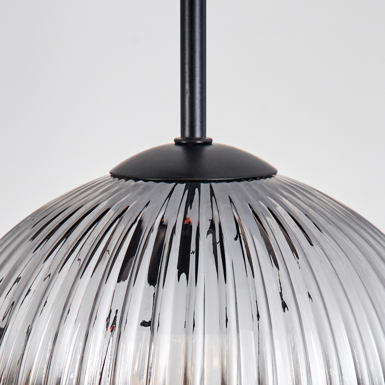Nahaufnahme eines Glasschirms mit vertikalen Rippen, schwarzen Metallteilen und weißem Hintergrund.