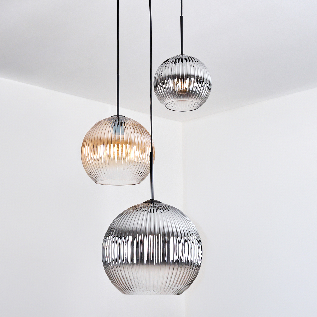 Drei Glashängeleuchten hängen von der Decke. Die Leuchten haben ein geripptes Design und unterschiedliche Farbtöne.