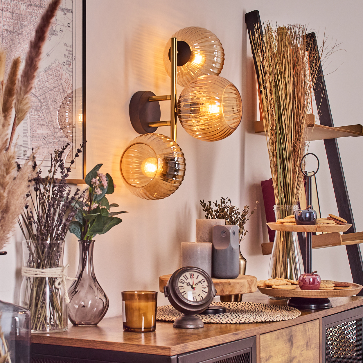 Ein Raum mit Lampe, Blumen, Uhr und Kerzen auf einem Schrank. An der Wand hängt eine Karte. Im Hintergrund ist eine Leiter.
