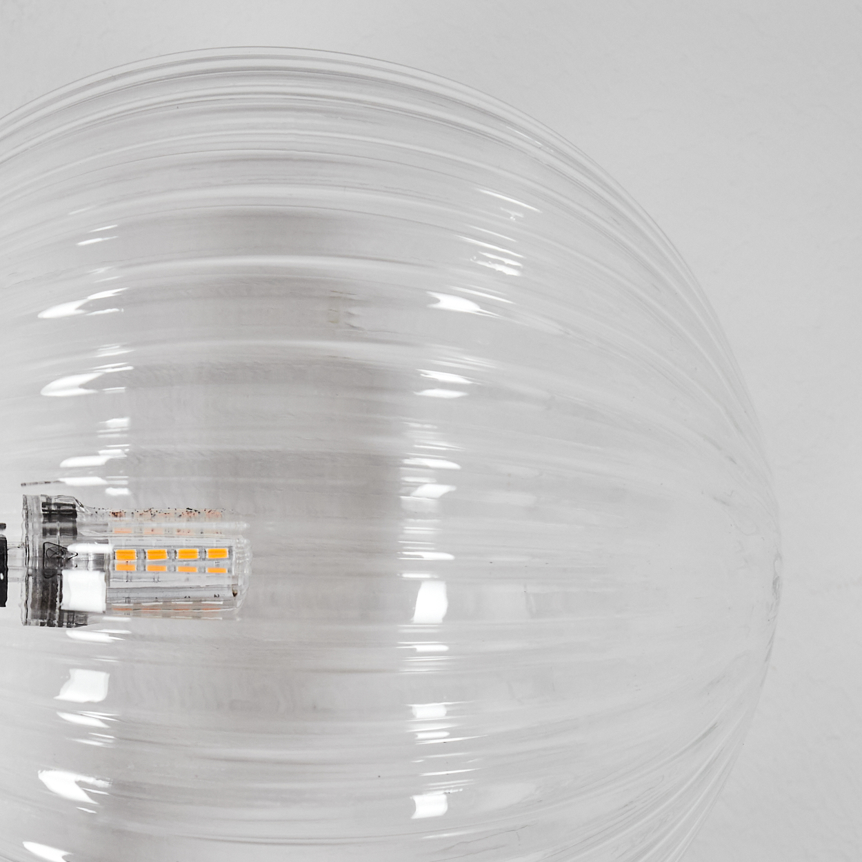 Eine klare, gerippte Glasbirne. Die Glühbirne ist teilweise mit orangen LEDs beleuchtet. Der Hintergrund ist weiß.