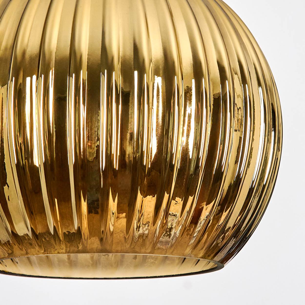 Nahaufnahme eines goldenen Glaslampenschirms mit vertikalen Rippen. Der Hintergrund ist weiß, und das Glas reflektiert Licht.
