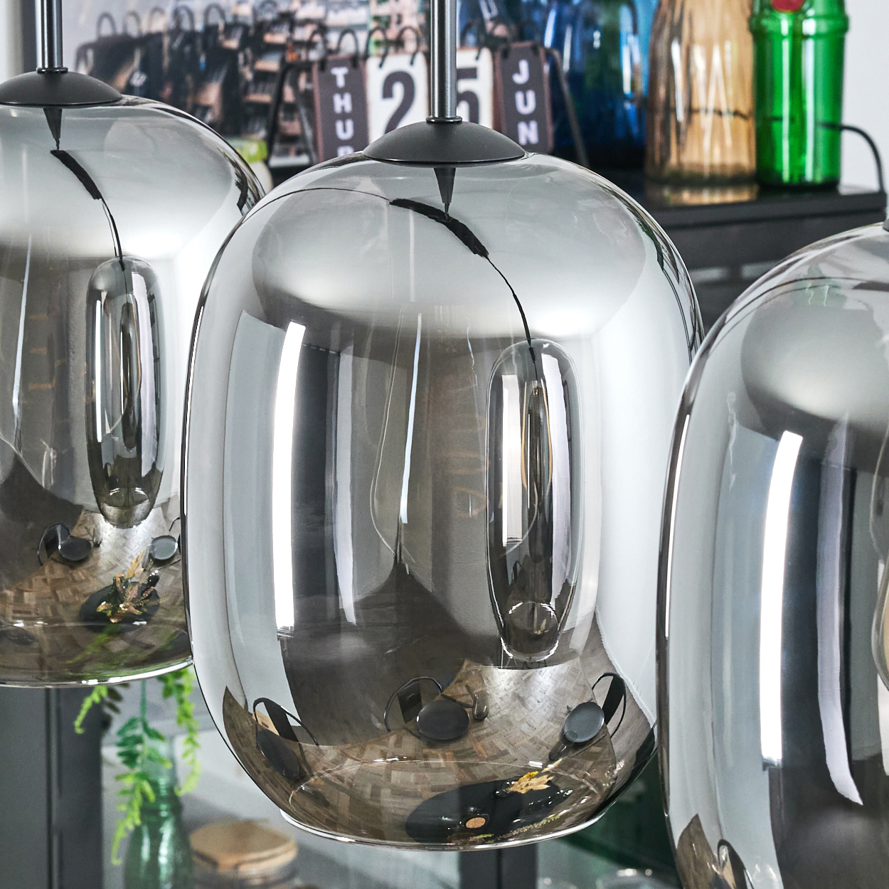 Drei hängende Pendelleuchten aus verspiegeltem Glas. Im Hintergrund sind ein Kalender und Glasflaschen zu sehen.