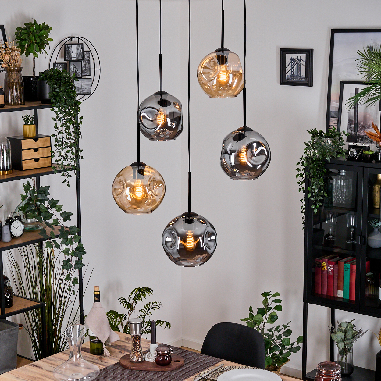 Esszimmer mit Hängelampen. Pflanzen, Holztisch, Regale und ein schwarzer Schrank. Die Lampen sind Glaskugeln.