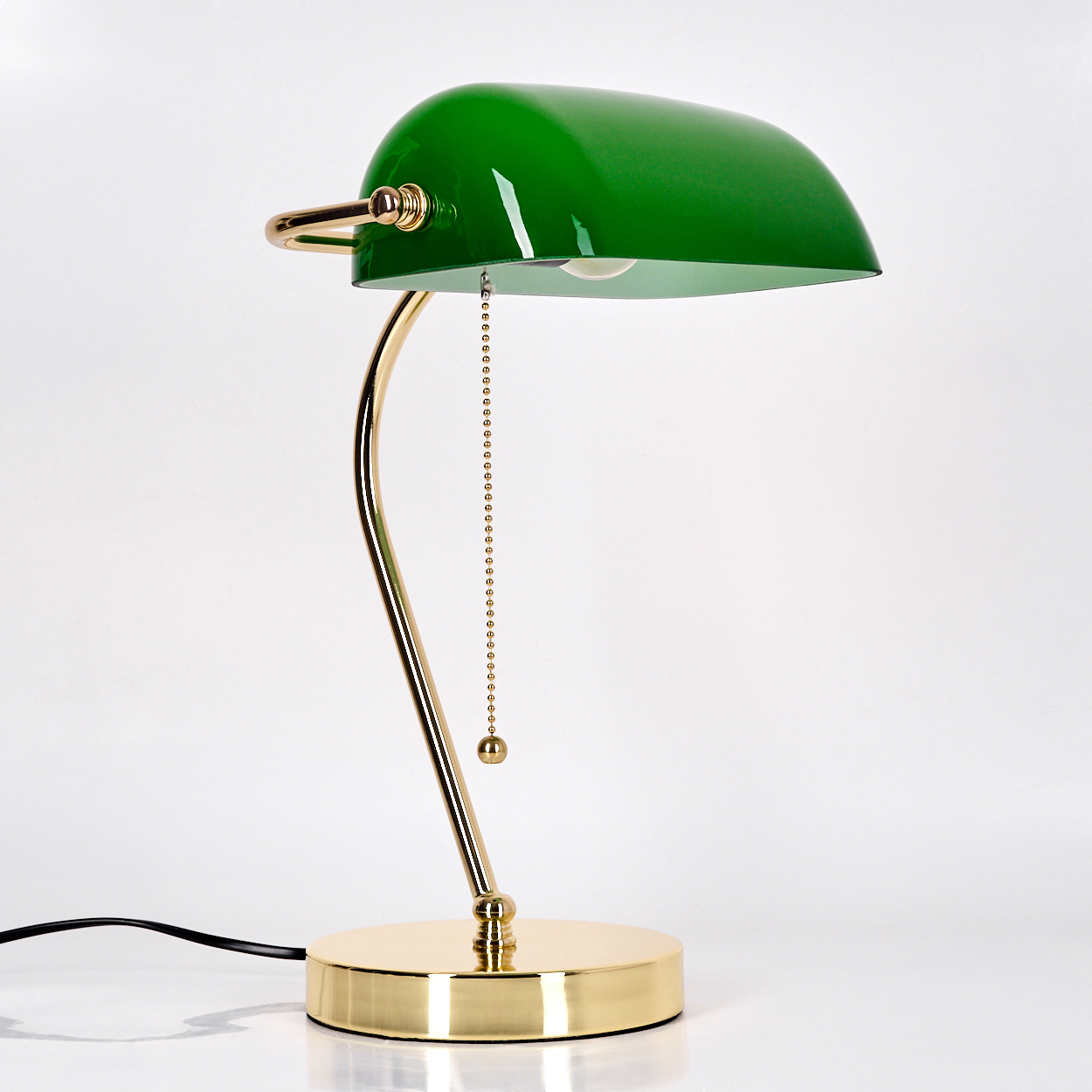 Eine grüne Banker-Lampe mit goldenem Fuß und Arm sowie einem schwarzen Netzkabel. Der Hintergrund ist weiß.