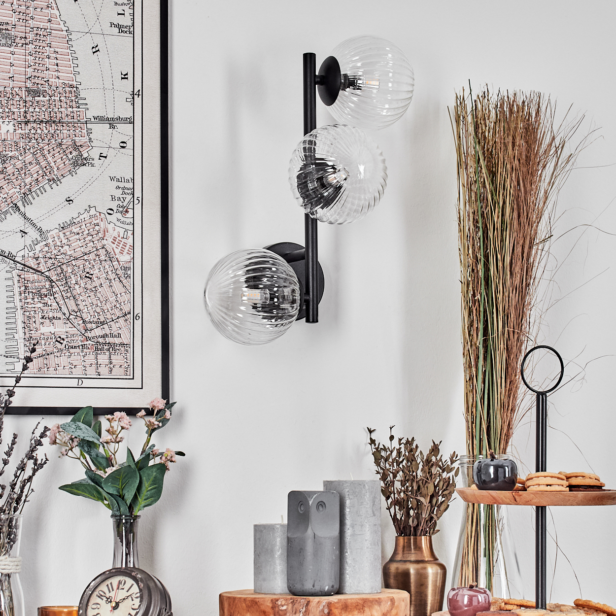 Eine Wand mit einer Karte und einer schwarzen Lampe mit drei klaren Glaskugelleuchten. Es gibt Dekorationen wie Blumen und Kekse.