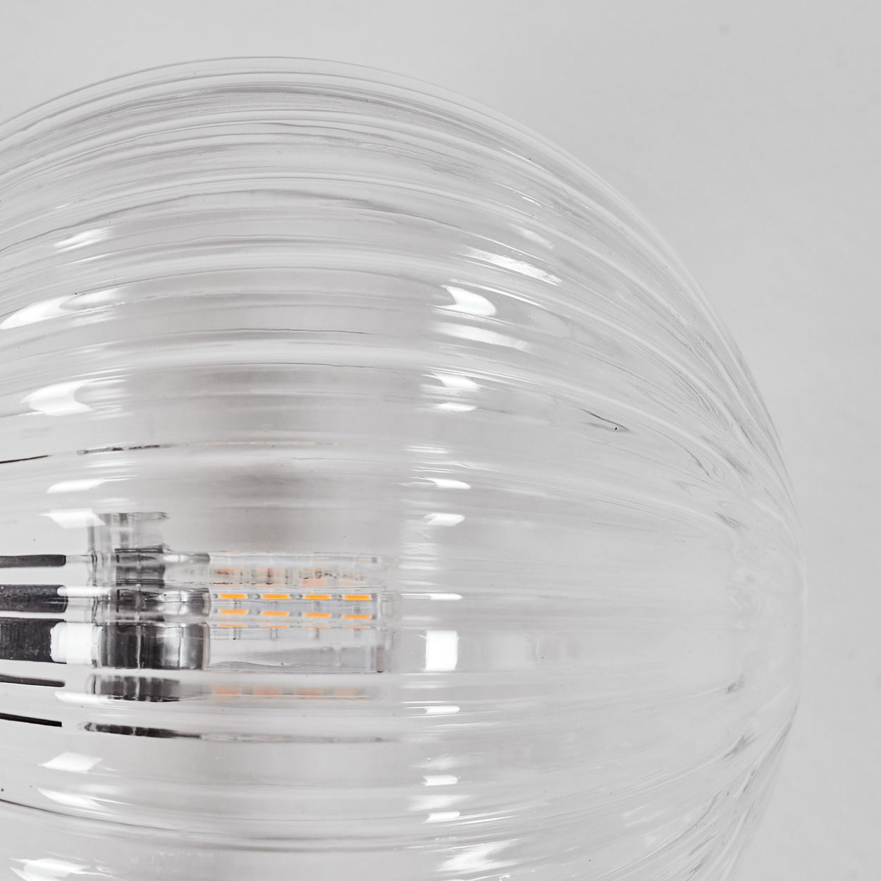 Nahaufnahme einer durchsichtigen Glasleuchte mit horizontalen Rippen. Die Leuchte enthält ein oranges LED-Licht. Weißer Hintergrund.