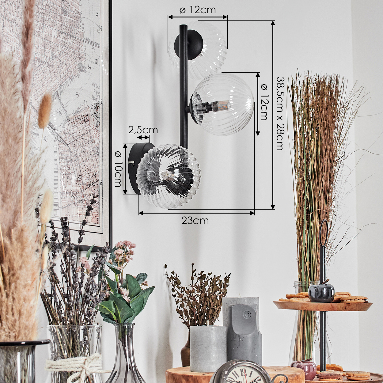 Eine moderne Wandlampe mit drei Glaskugeln. Verschiedene dekorative Gegenstände, darunter Blumen, Vasen und eine Karte, befinden sich im Vordergrund.