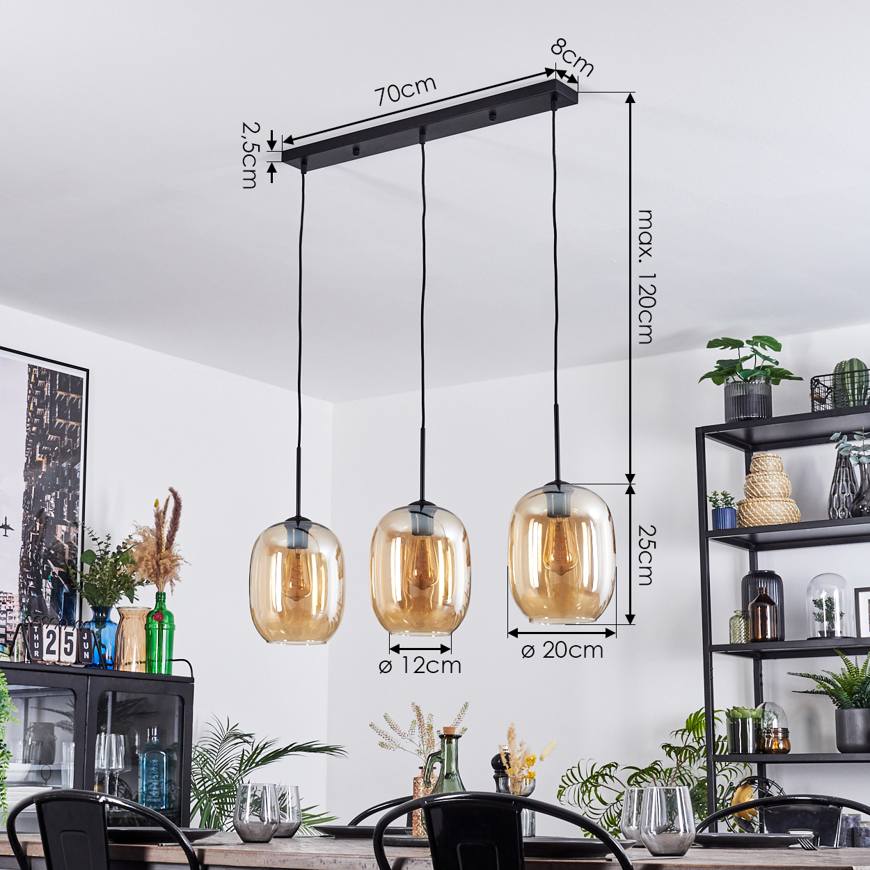Drei Pendelleuchten mit bernsteinfarbenen Glasschirmen hängen über einem Tisch. Rechts ein schwarzes Metallregal mit Pflanzen.