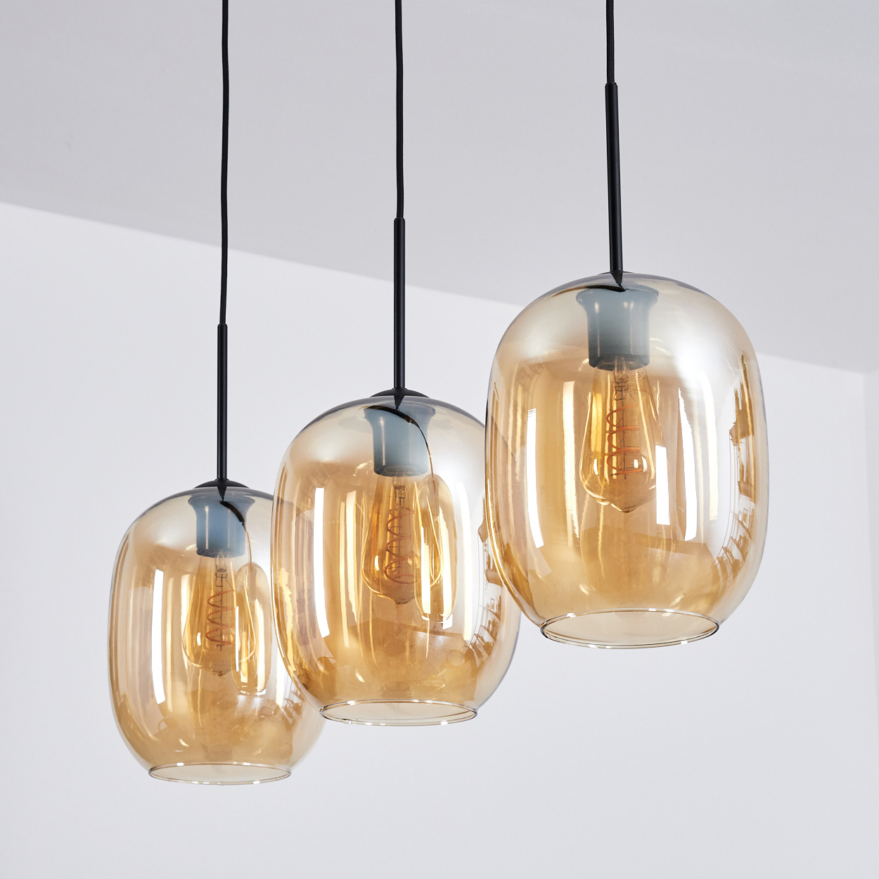 Drei Pendelleuchten mit bernsteinfarbenen Glasschirmen und Edison-Glühbirnen hängen an schwarzen Kabeln.