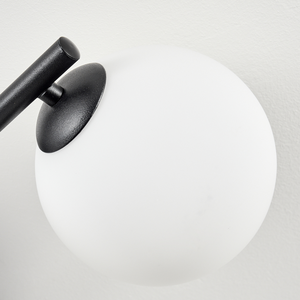 Nahaufnahme einer modernen Lampe. Sie hat einen großen, weißen Globus, der an einem schwarzen Metallarm befestigt ist, vor einer weißen Wand.