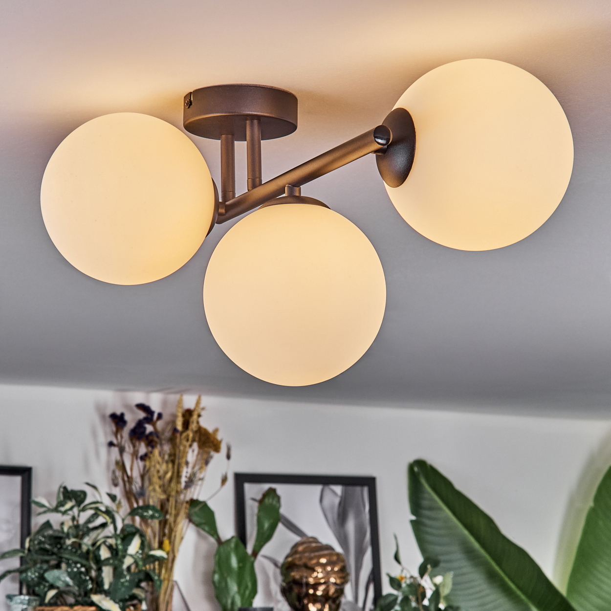 Moderne Deckenleuchte mit drei kugelförmigen Lampen. Darunter Pflanzen und gerahmte Kunst, die den Raum gemütlich gestalten.