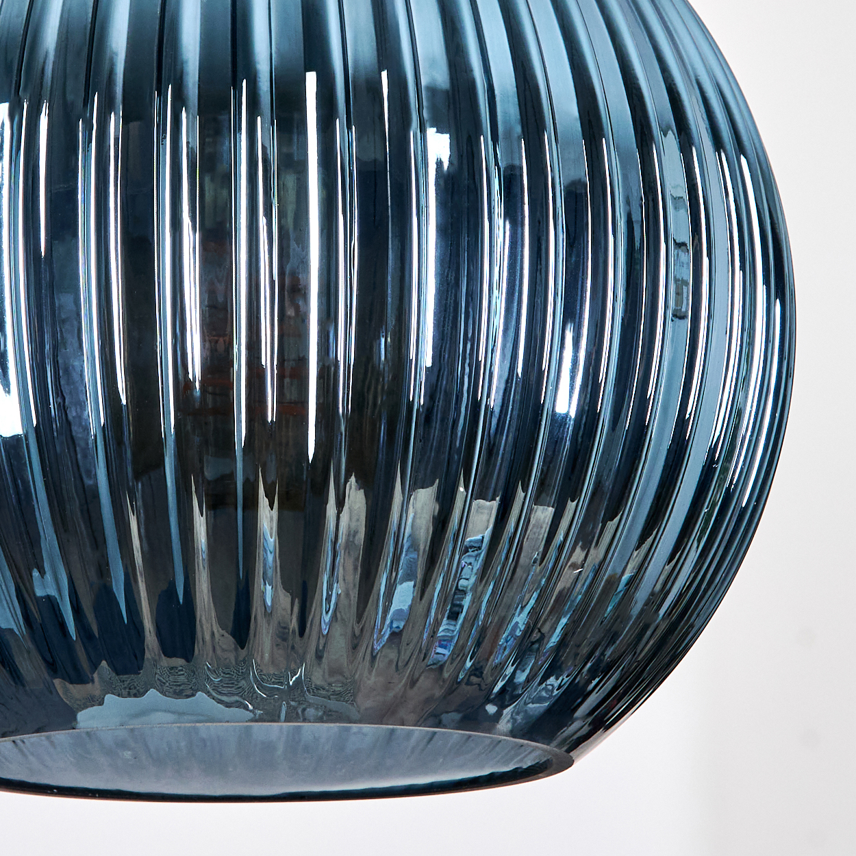 Nahaufnahme eines blauen Glasobjekts mit vertikalen Rippen. Das Glas reflektiert Licht. Der Hintergrund ist weiß.