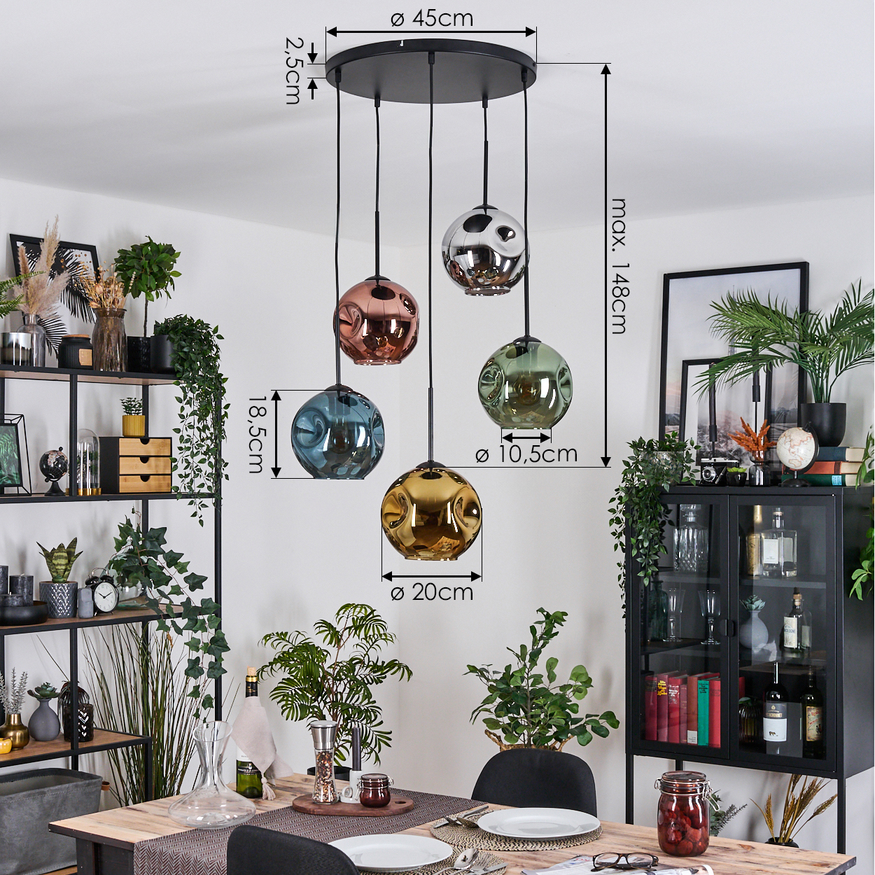 Ein Esszimmer mit einem schwarzen Kronleuchter mit fünf farbigen Glaskugelleuchten. Regale, Pflanzen und ein Tisch sind ebenfalls sichtbar.