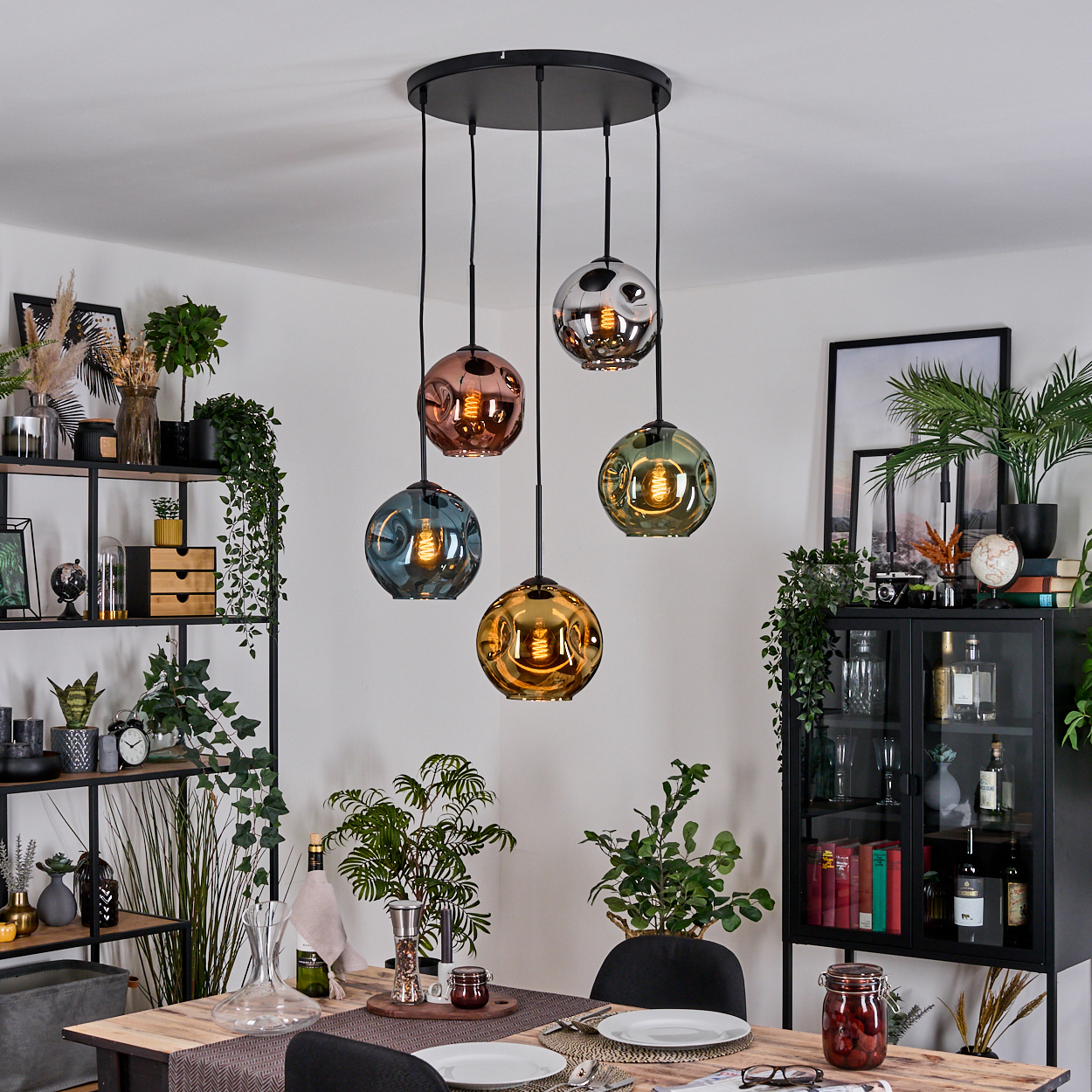 Esszimmer mit Holztisch, Hängelampen, Pflanzen und einem schwarzen Schrank. Die Lampen sind in verschiedenen Farben.