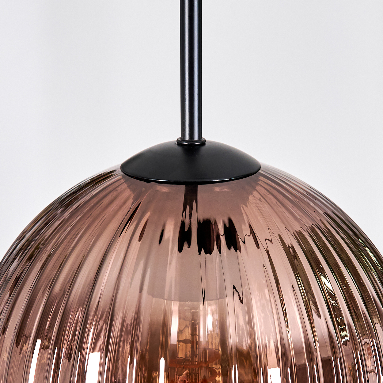 Nahaufnahme einer stilvollen Pendelleuchte. Die Lampe hat einen braunen, gerippten Glasschirm und eine schwarze Metallbefestigung. Weißer Hintergrund.