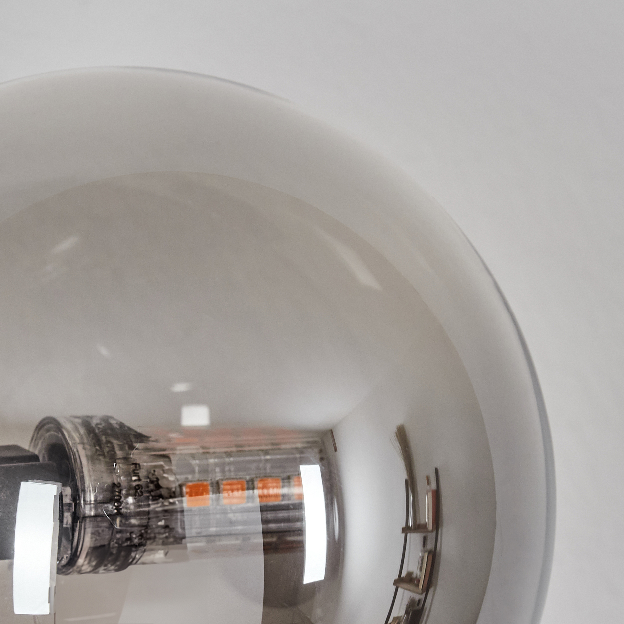 Nahaufnahme einer Glühbirne. Das Glas der Glühbirne ist grau. Im Inneren ist eine orangefarbene LED sichtbar. Eine kleine Leiter spiegelt sich.