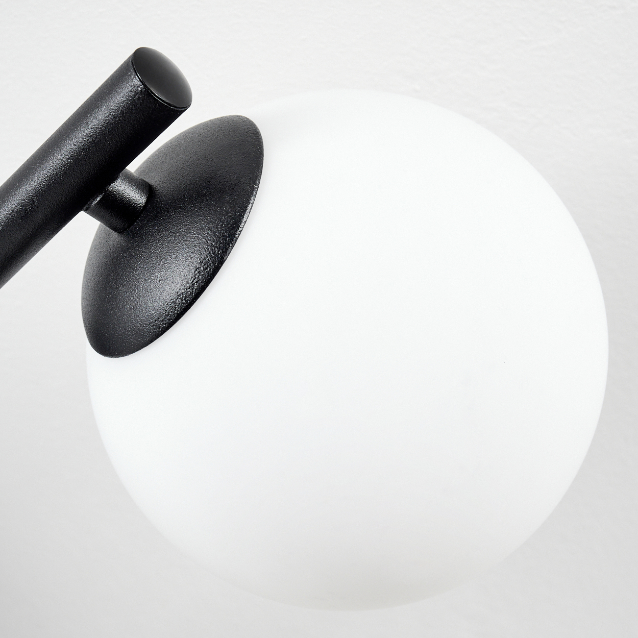 Nahaufnahme einer modernen Lampe. Ein schwarzer Metallarm trägt einen weißen, kugelförmigen Lampenschirm auf weißem Hintergrund.