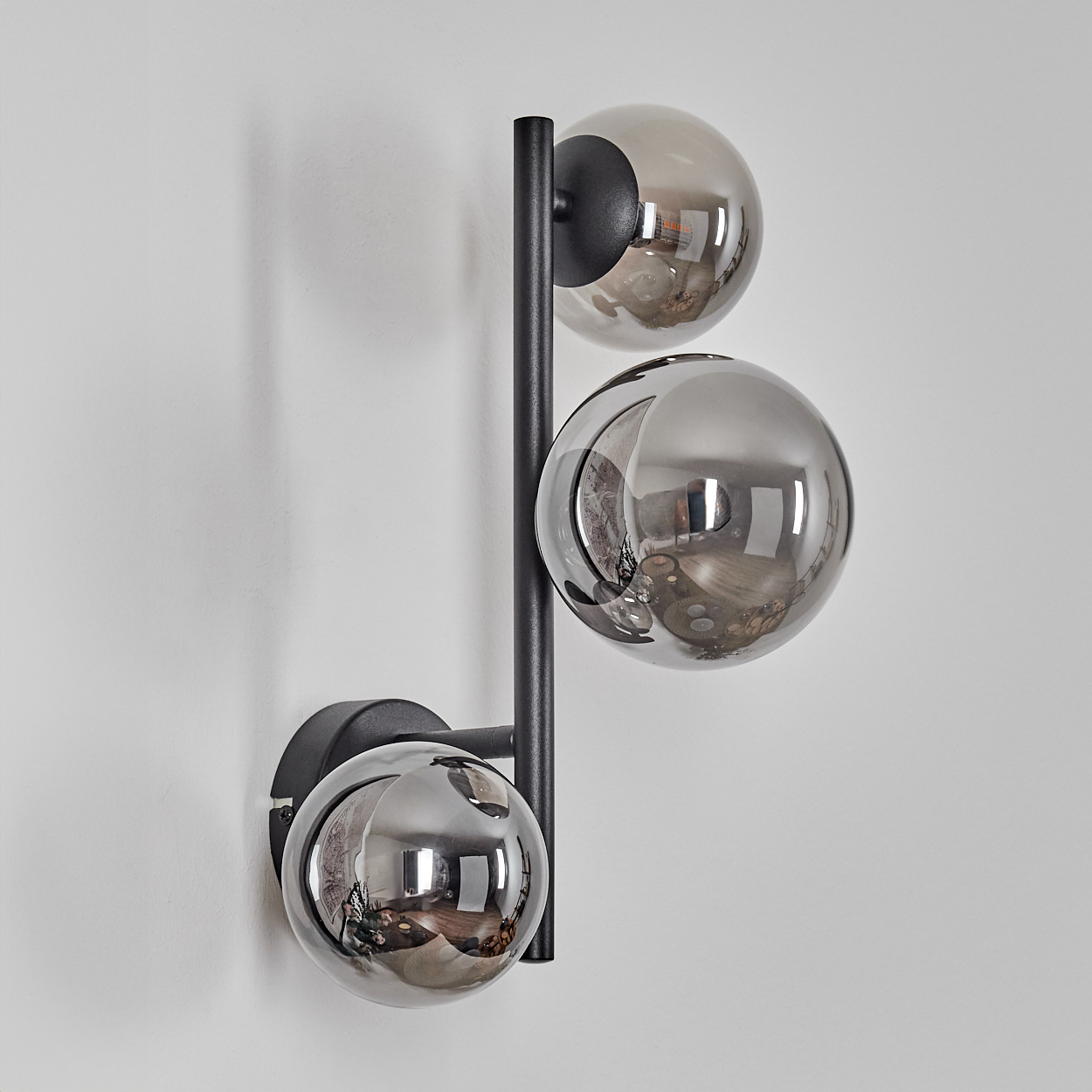 Eine moderne Wandlampe mit drei kugelförmigen Schirmen. Die Schirme sind reflektierend und die Halterung ist schwarz, an einer weißen Wand befestigt.