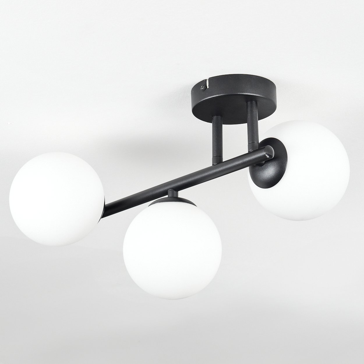 Eine moderne Deckenleuchte mit drei weißen kugelförmigen Lampen und schwarzen Metallarmen, die an einer weißen Decke befestigt ist.