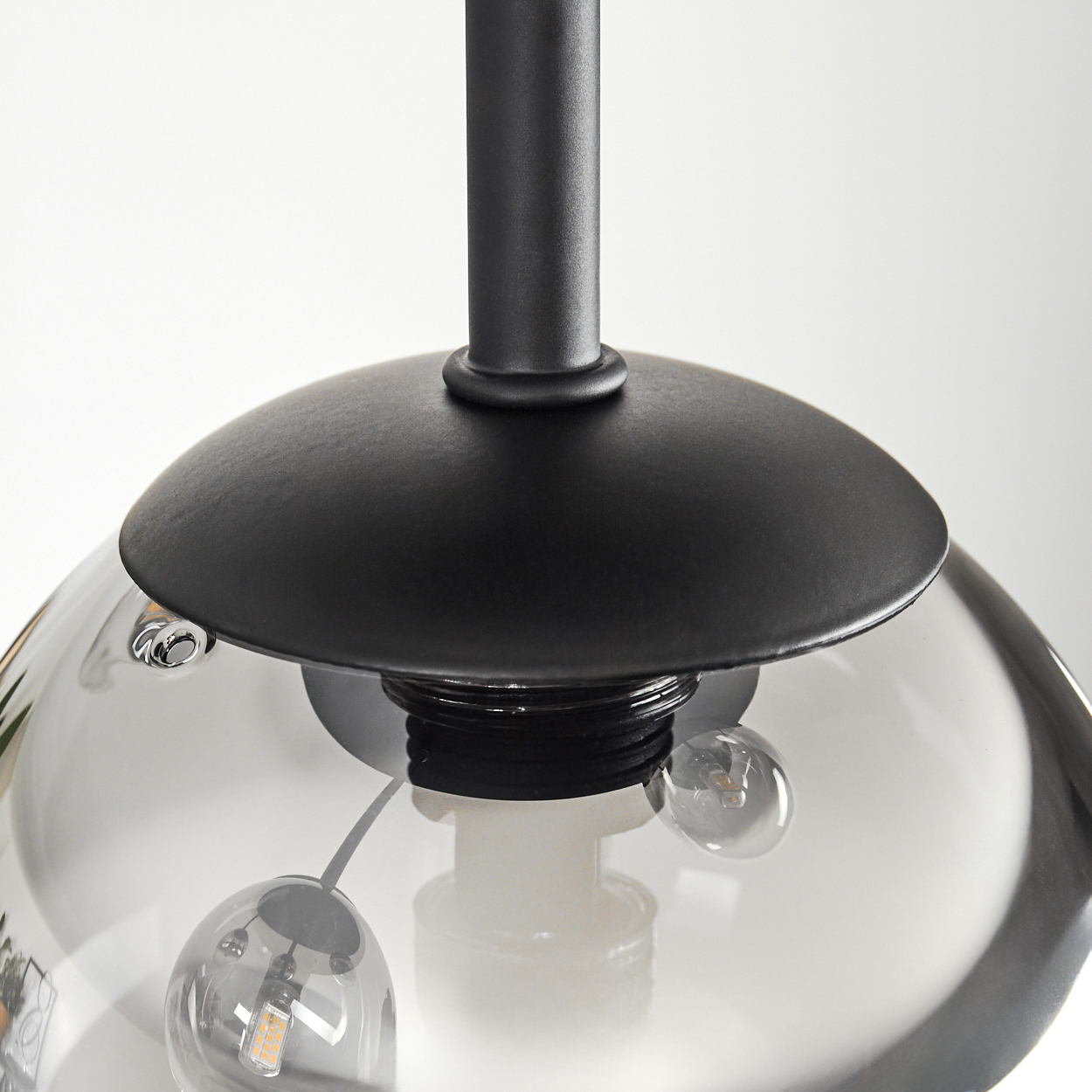 Nahaufnahme einer schwarzen Pendelleuchte. Ein klarer Glasschirm mit zwei kleinen Glühbirnen und eine schwarze Metallstange und ein Baldachin sind sichtbar.
