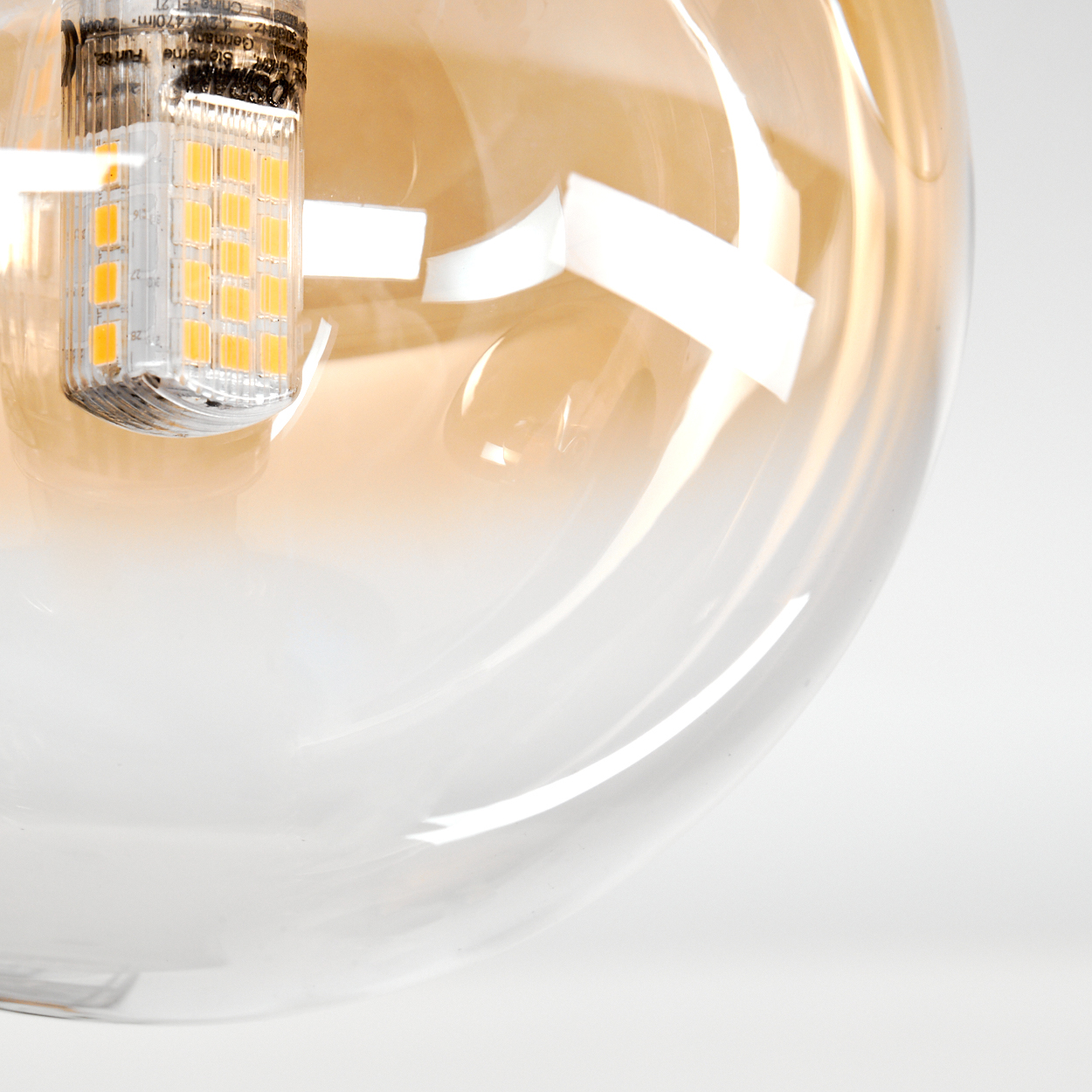 Nahaufnahme einer Glühbirne. Die Birne ist rund und transparent, mit gelb-oranger Tönung. Im Inneren befindet sich eine kleine LED-Leuchte.