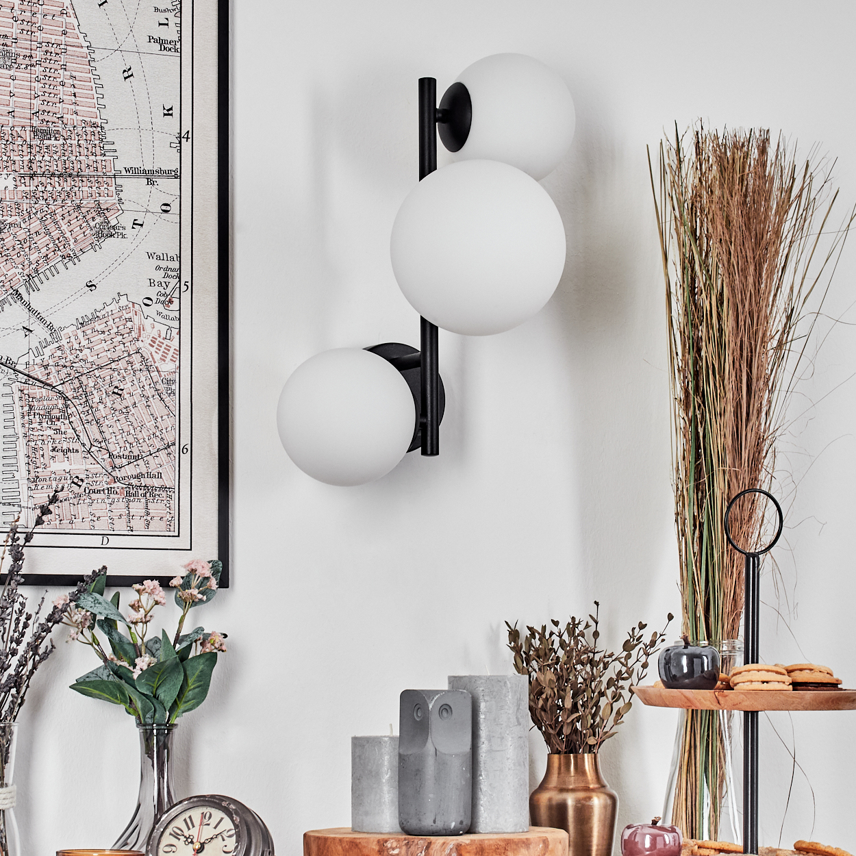 Eine moderne Wandlampe mit drei weißen Kugeln. Eine Karte, Blumen, Kerzen und Dekorationen an einer weißen Wand.