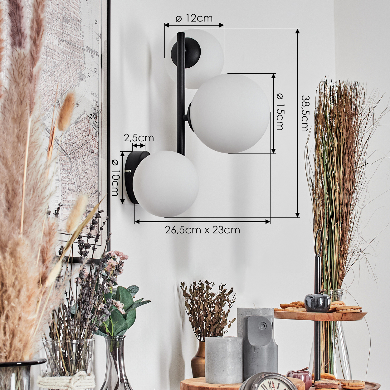 Eine moderne Wandlampe mit drei weißen Kugeln. Getrocknete Pflanzen und verschiedene Dekorationsartikel sind im Vordergrund. Abmessungen sind angegeben.