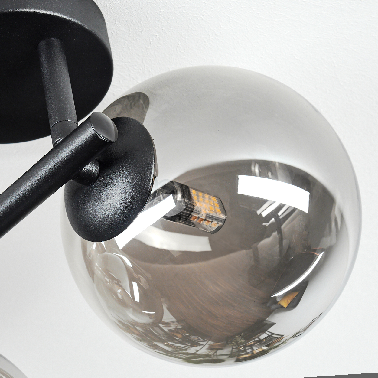 Eine moderne schwarze Metalllampe mit einem grauen Glaskugel, die die Umgebung reflektiert. Die Lampe ist auf einer weißen Oberfläche montiert.